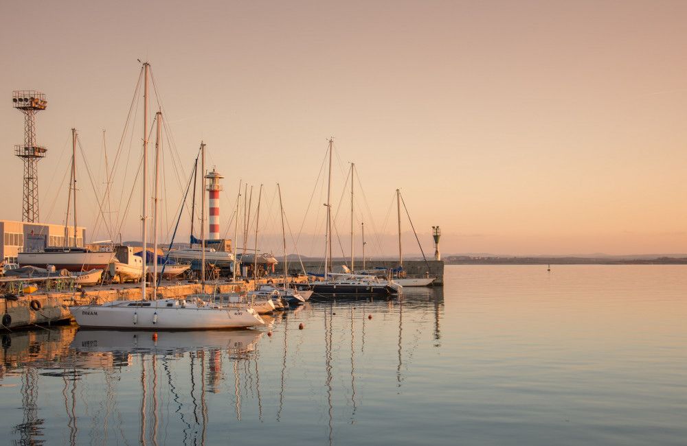 Sailboats docked at sea marina with lighthouse in background at dusk