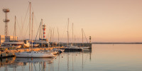 Sailboats docked at sea marina with lighthouse in background at dusk