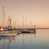 Sailboats docked at sea marina with lighthouse in background at dusk
