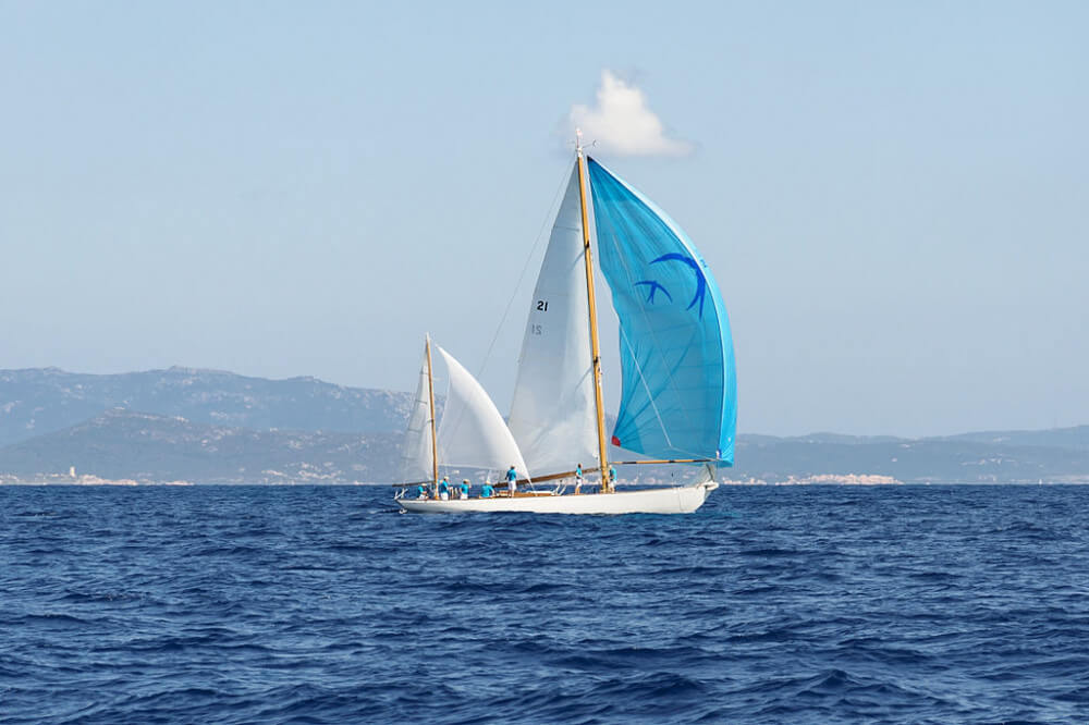 White yawl with white sails and bright blue spinnaker on Medditerrenean