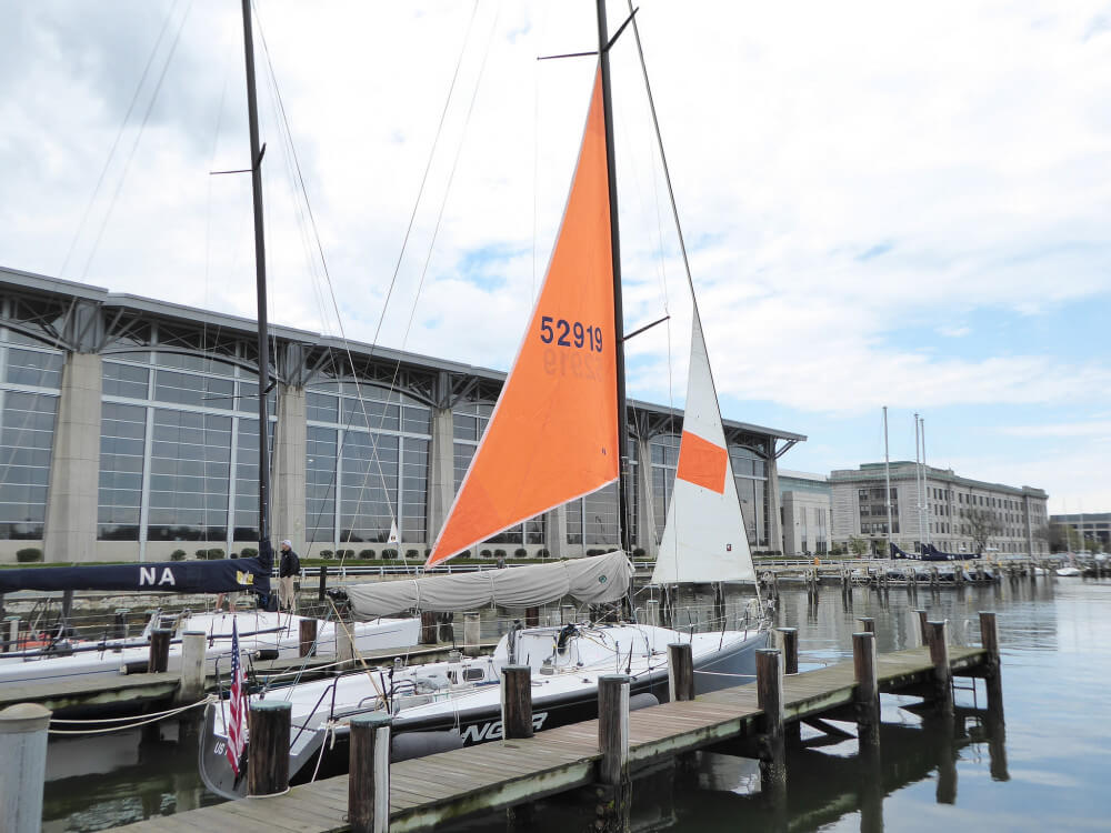 US naval acadamy sloop in marina with bright orange storm trysail and stormjob