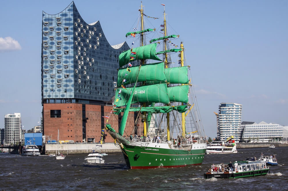 Green tall ship with green square rigged sails against urban background
