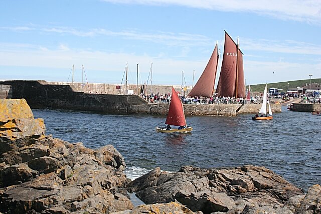 Lugger sails behind berth with rocks and small sloops in the foreground