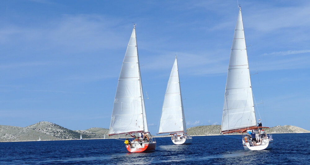 Three sailboats racing on lake with some hills in the background