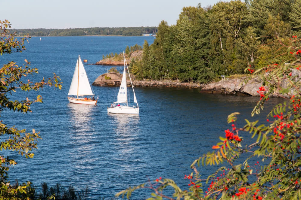 Two sailboats sailing on al lake with lots of trees around