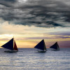 3 Sailboats with dark sails under dark clouds at sunset
