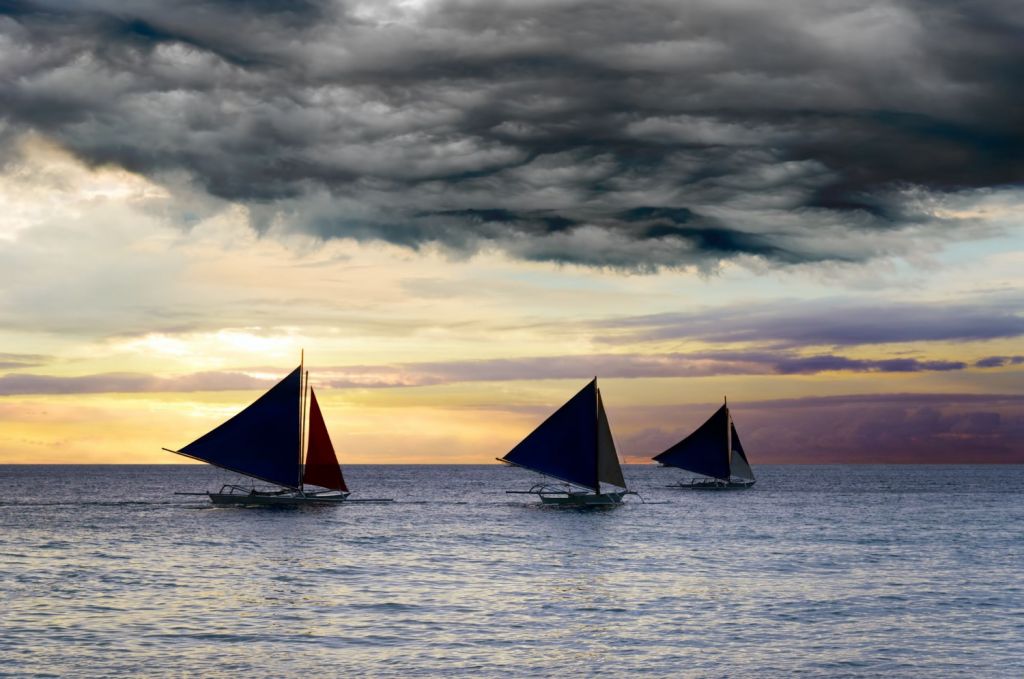 3 Sailboats with dark sails under dark clouds at sunset