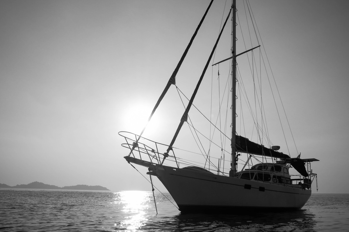 Cutter motorsailor against sun in black and white