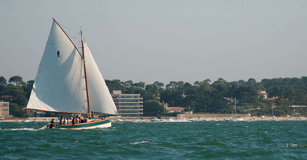 Gaff Rigged Sloop in white in front of coastline with flat