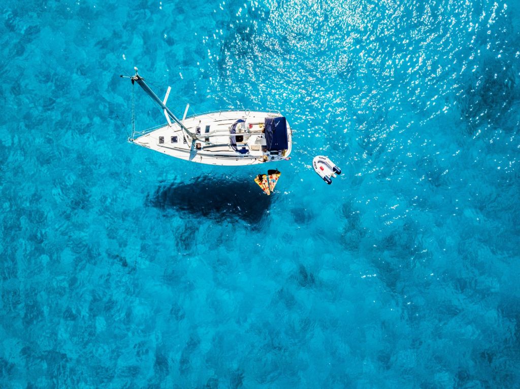 A sailboat at anchor from above in clear blue waters