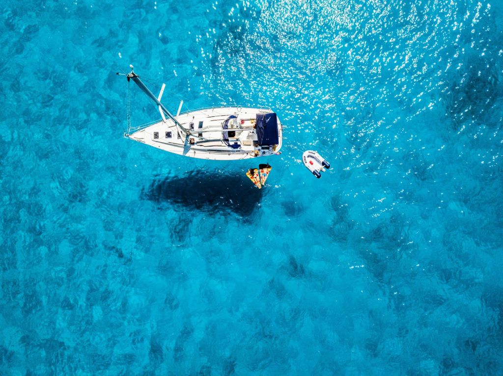 A sailboat at anchor from above in clear blue waters