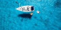A sailboat at anchor from above in clear blue waters